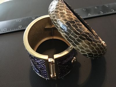Sale Photo Thumbnail #98: Lot of two fashion bracelets featuring snakeskin texturing. Includes one wide gold-tone hinged cuff bracelet with purple snakeskin-style inlay and gold-tone stud accents, and one rounded slip-on bangle bracelet with neutral gray and brown snakeskin patter