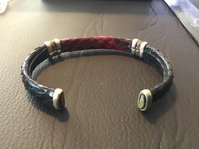 Sale Photo Thumbnail #13: An open cuff bracelet featuring red and dark navy/black snakeskin leather trim with metallic end caps and decorative band accents. Shows light wear consistent with pre-owned use.
