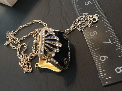 Sale Photo Thumbnail #57: gold-tone chain necklace featuring an ornate purse-shaped locket pendant with black enamel work and clear rhinestone accents. The locket opens on a bottom hinge with a textured gold-tone interior. Pendant measures approximately 1.5 inches wide by 1.25 inc