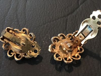 Sale Photo Thumbnail #87: Pair of vintage clip-on earrings featuring Shell cameo portrait  set within ornate, filigree-style gold-tone metal frames. The clips show some age-related patina and finish wear on the reverse side. Overall good vintage condition.