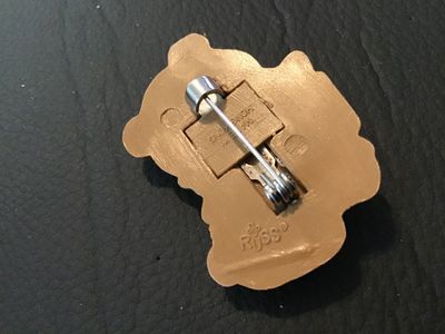 Sale Photo Thumbnail #56: Vintage Christmas-themed teddy bear pin or brooch by Russ. Made of molded painted plastic, featuring a teddy bear holding a wrapped present with holly leaf details. Marked 'Russ' and 'Made in Hong Kong' on the back. Pin mechanism is intact and functional.