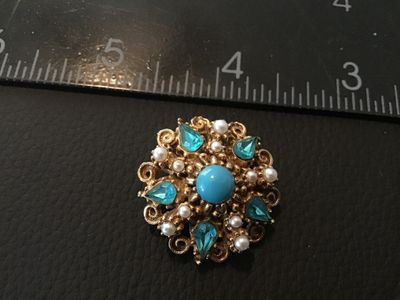 Sale Photo Thumbnail #6: A vintage ornate gold-tone brooch/pin by Florenza featuring a central faux turquoise cabochon surrounded by faux pearls and teardrop light blue rhinestones. Filigree/scrollwork detailing on a textured gold-tone setting. Signed FLORENZA© on the back. Meas