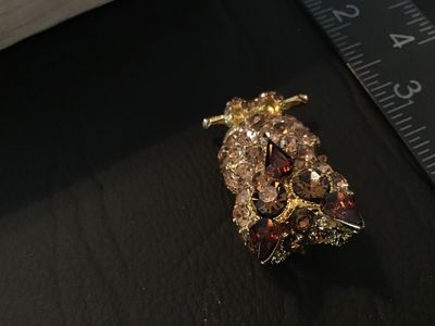 Sale Photo Thumbnail #32: Gold tone owl-shaped brooch featuring paved brown and champagne-colored rhinestones with dark amber glass accents for the ears and beak. Measures approximately 1.5 inches in length. Features a rollover safety clasp on the back. Good pre-owned condition wi