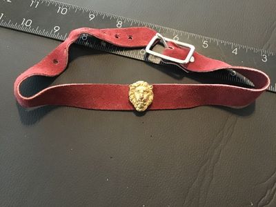Sale Photo Thumbnail #110: Vintage burgundy red suede leather choker or belt-style band featuring a gold-tone lion head medallion at the center. Secured with a silver-tone buckle closure and screw-back attachment for the charm. Measures approximately 12 to 14 inches long. Shows lig