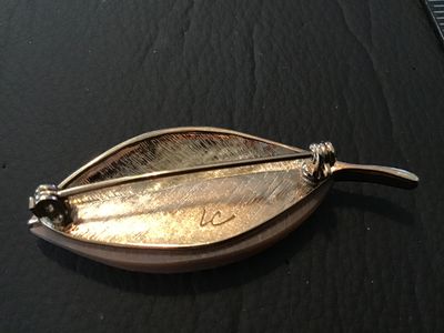 Sale Photo Thumbnail #71: A vintage Liz Claiborne leaf brooch featuring a gold-tone metal half with detailed veining and a iridescent mother-of-pearl (or shell inlay) half. Signed 'LC' on the back. Measures approximately 2.25 inches long. Features a standard rollover safety clasp 