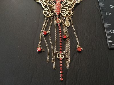 Sale Photo Thumbnail #38: Statement necklace featuring a large openwork butterfly focal piece adorned with red rhinestones and hanging chain fringe with rhinestone drops. Marked 'PILGRIM' on the back of the butterfly and 'DANISH DESIGN' on the metal tag near the clasp. Features a 