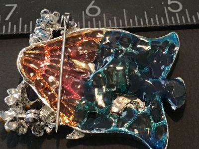 Sale Photo Thumbnail #91: Silver-tone bell-shaped brooch pin featuring colorful enamel artwork depicting two white swans in a pond setting with cattails and floral accents. Translucent stained glass-style back in shades of teal, orange, and blue. Measures approximately 2 inches wi