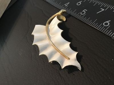 Sale Photo Thumbnail #63: A vintage white enamel and gold-tone metal brooch styled as a ruffled leaf. Features a textured gold-tone back with a standard pin stem and rollover safety clasp. Measures approximately 2.5 inches long. Pre-owned condition with minor signs of surface wear