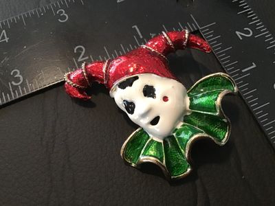 Sale Photo Thumbnail #76: Vintage enamel clown or jester face brooch pin featuring bold red, green, and white enamel details over a gold-tone textured metal setting. Measures approximately 2 inches wide by 2 inches tall. Features a standard rolling C-clasp on the back. Good pre-ow