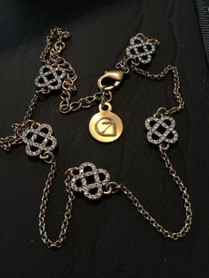 Sale Photo Thumbnail #64: Gold-tone chain necklace featuring openwork, Celtic knot-style stations encrusted with clear rhinestones. Includes a lobster claw clasp with an adjustable extender chain and a signature round logo hangtag with a stylized '7' or leaf design. Gently used co