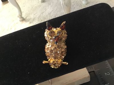 Sale Photo Thumbnail #30: Gold tone owl-shaped brooch featuring paved brown and champagne-colored rhinestones with dark amber glass accents for the ears and beak. Measures approximately 1.5 inches in length. Features a rollover safety clasp on the back. Good pre-owned condition wi