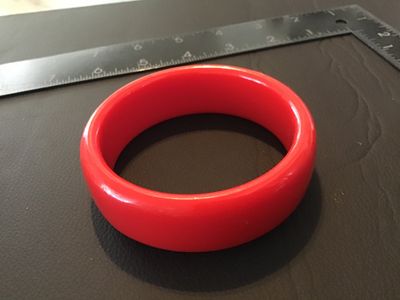 Sale Photo Thumbnail #106: Thick bright red plastic or resin bangle bracelet. Measures approximately 2.5 inches in interior diameter and roughly 0.75 inches wide. Good pre-owned condition with minor surface wear visible upon close inspection.