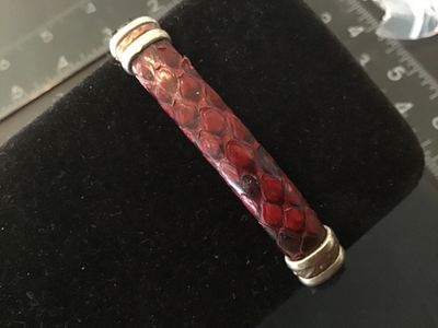 Sale Photo Thumbnail #12: An open cuff bracelet featuring red and dark navy/black snakeskin leather trim with metallic end caps and decorative band accents. Shows light wear consistent with pre-owned use.