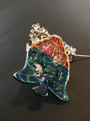 Sale Photo Thumbnail #89: Silver-tone bell-shaped brooch pin featuring colorful enamel artwork depicting two white swans in a pond setting with cattails and floral accents. Translucent stained glass-style back in shades of teal, orange, and blue. Measures approximately 2 inches wi