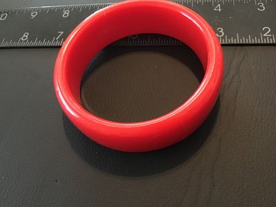 Sale Photo Thumbnail #107: Thick bright red plastic or resin bangle bracelet. Measures approximately 2.5 inches in interior diameter and roughly 0.75 inches wide. Good pre-owned condition with minor surface wear visible upon close inspection.