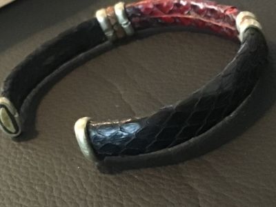 Sale Photo Thumbnail #15: An open cuff bracelet featuring red and dark navy/black snakeskin leather trim with metallic end caps and decorative band accents. Shows light wear consistent with pre-owned use.