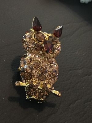Sale Photo Thumbnail #33: Gold tone owl-shaped brooch featuring paved brown and champagne-colored rhinestones with dark amber glass accents for the ears and beak. Measures approximately 1.5 inches in length. Features a rollover safety clasp on the back. Good pre-owned condition wi