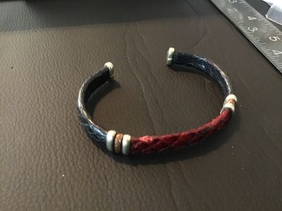 Sale Photo Thumbnail #14: An open cuff bracelet featuring red and dark navy/black snakeskin leather trim with metallic end caps and decorative band accents. Shows light wear consistent with pre-owned use.