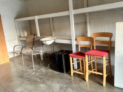 Sale Photo Thumbnail #37: Collection of basement and outdoor items including a pair of wooden barstools with red seats, outdoor mesh armchairs, a small black compact refrigerator, and a decorative birdbath stand.