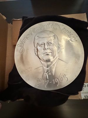 Sale Photo Thumbnail #22: Commemorative John F. Kennedy silver-tone metal plate featuring a bas-relief portrait and dates 1917–1963, housed in its original box with black fabric backing.