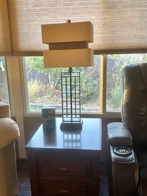 Sale Photo Thumbnail #19: Modern table lamp featuring an open metal grid stem and a tiered beige fabric shade, set on a dark wood end table with drawers.