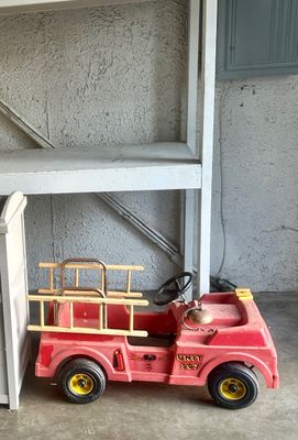 Sale Photo Thumbnail #3: Vintage red plastic ride-on pedal fire truck featuring wooden side ladders, a front bell, and black wheels.