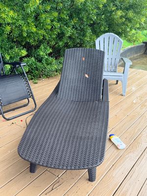Sale Photo Thumbnail #60: Dark brown woven resin wicker lounge chair on a wooden deck, flanked by a grey plastic Adirondack chair and a black folding zero gravity chair.