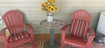 Sale Photo Thumbnail #10: Pair of red plastic Adirondack patio chairs with striped cushions, paired with a small round mosaic-top accent table topped with a milk can arrangement of faux sunflowers.