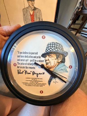 Sale Photo Thumbnail #39: Vintage Paul "Bear" Bryant commemorative wall clock with a black frame, featuring an illustration, quote, and career stats.