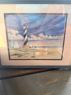 Sale Photo Thumbnail #66: Framed watercolor print depicting the Cape Hatteras Lighthouse against a cloudy sky, presented in a mat and dark wooden frame under glass.