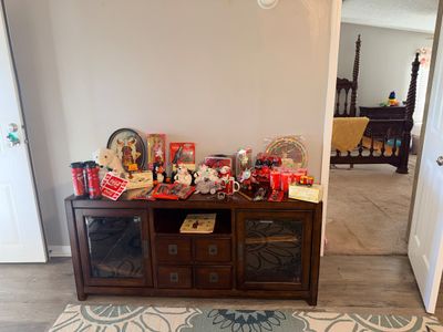 Sale Photo Thumbnail #7: Collection of Coca-Cola collectibles including plush polar bears, trays, glasses, and tin signs, displayed on a dark wood media console.