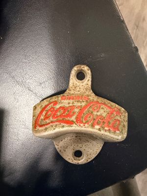 Sale Photo Thumbnail #17: Vintage cast metal wall-mounted Coca-Cola bottle opener featuring embossed red lettering with noticeable surface wear and patina.
