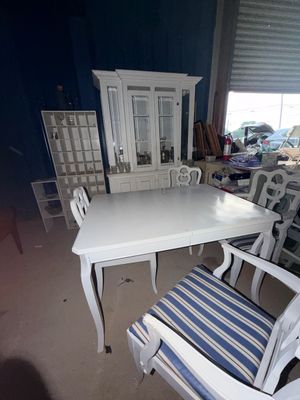 Sale Photo Thumbnail #61: White-painted dining table set with blue-and-white striped upholstered chairs, alongside a matching hutch and cubby shelving unit in a warehouse setting.