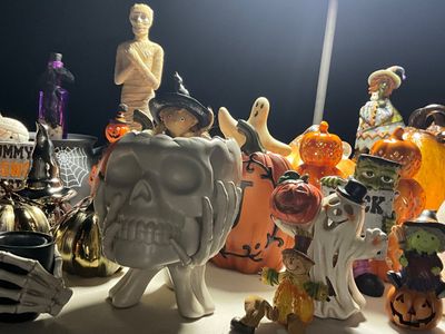 Sale Photo Thumbnail #24: Collection of Halloween decorations including a matte white skull bowl, mummy figurine, ceramic ghosts, witches, and pumpkins.
