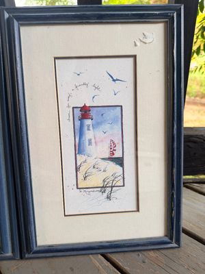 Sale Photo Thumbnail #62: Framed lighthouse watercolor print by D. Morgan, dated 1994, featuring handwritten text 'from far away, a friendly light' in a dark blue wooden frame.