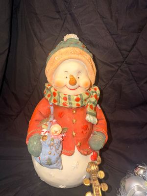 Sale Photo Thumbnail #27: Painted resin snowman figurine featuring a knit-textured hat, red coat, patterned scarf, and a shoulder bag holding a miniature snowman.