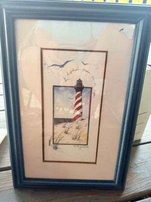 Sale Photo Thumbnail #64: Framed nautical art print by D. Morgan depicting a red-and-white spiral striped lighthouse on a sandy beach, presented under glass in a dark wooden frame.