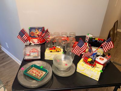 Sale Photo Thumbnail #4: Collection of vintage Coca-Cola memorabilia, including glassware, tin trays, die-cast Matchbox vehicles, and decorative items alongside clear glass dishware.