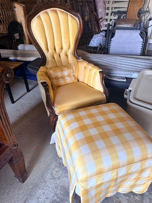 Sale Photo Thumbnail #57: Vintage Victorian-style high-back armchair in carved dark wood with tufted yellow fabric upholstery, matching accent pillow, and a yellow gingham skirted ottoman.