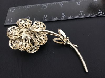 Sale Photo Thumbnail #155: Vintage gold-tone flower brooch by Sarah Coventry featuring ornate filigree work accenting pink/fuchsia aurora borealis rhinestones. Signed "© SARAH COV" on the back stem. Features a secure pin back clasp. Measures approximately 3 inches long. In good vi