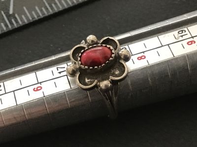 Sale Photo Thumbnail #75: Vintage Southwestern style silver ring featuring a central red stone cabochon set in a saw-tooth bezel with scalloped and bead accents. Shown on a ring mandrel as approximately size 7. Features a split-shank band design. Shows minor surface wear and natur