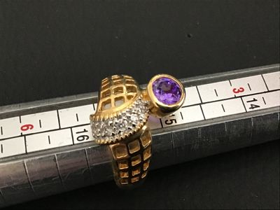 Sale Photo Thumbnail #240: A distinctive gold-tone statement ring featuring a bypass-style lattice/grid design, accent stones along the band, and a bezel-set purple round stone. Shown on a ring mandrel measuring approximately size 6 to 6.5. Good condition with light surface wear.