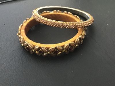 Sale Photo Thumbnail #133: Set of two statement bangle bracelets featuring yellow thread wrapping. One wider bangle is adorned with gold-tone leaf accents, pink/red and green rhinestones, and faux pearl details. The second thinner bangle features full rows of shimmering champagne/g