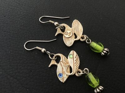 Sale Photo Thumbnail #62: Pair of vintage Signed  Jewelry) silvertone/goldtone fish dangle pierced earrings. Feature textured dual fish motifs set with small blue and green rhinestone eyes, accented with dangling green glass beads and fluted metal beads. The back is marked with th