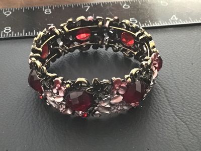 Sale Photo Thumbnail #86: A ornate stretch cuff bracelet featuring antiqued brass-tone metal set with large faceted red glass or acrylic stones, accent rhinestones, and delicate enameling on floral motifs in shades of pink, white, and grey. The bracelet features an elastic stretch