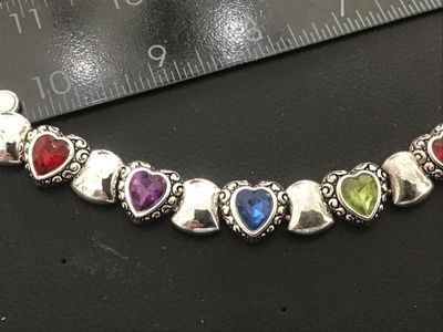 Sale Photo Thumbnail #64: Silver-tone costume jewelry link bracelet featuring heart-shaped scrollwork links set with vibrant multi-colored heart crystals (red, purple, blue, green). Measures approximately 7.5 to 8 inches in length. In good condition with light surface wear.
