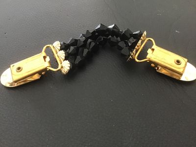Sale Photo Thumbnail #127: A vintage dress or cardigan clip featuring three strands of faceted black beads connected by gold-tone metal alligator clips with decorative end caps. Designed to hold cardigans, shawls, or cinch dresses. Shows minor surface wear consistent with age, but 