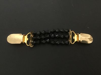 Sale Photo Thumbnail #126: A vintage dress or cardigan clip featuring three strands of faceted black beads connected by gold-tone metal alligator clips with decorative end caps. Designed to hold cardigans, shawls, or cinch dresses. Shows minor surface wear consistent with age, but 