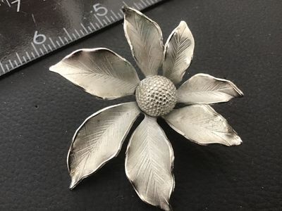 Sale Photo Thumbnail #123: A vintage silver-tone floral brooch Signed  featuring textured, vein-detailed leaves surrounding a domed, textured center. Marked on the back with the copyright Sarah Cov signature. Measures approximately 2 inches wide. Shows minor vintage surface wear co