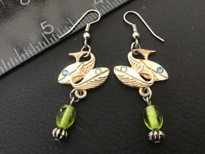 Sale Photo Thumbnail #60: Pair of vintage Signed  Jewelry) silvertone/goldtone fish dangle pierced earrings. Feature textured dual fish motifs set with small blue and green rhinestone eyes, accented with dangling green glass beads and fluted metal beads. The back is marked with th